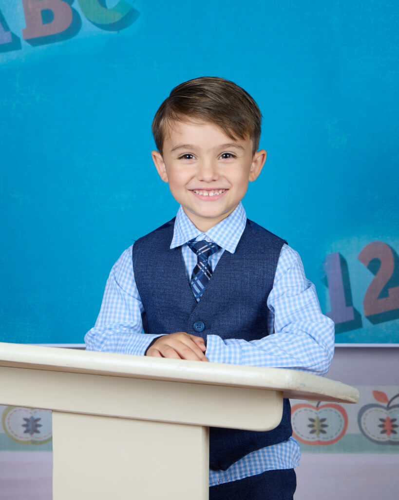 Smiling preschool boy posed at school desk during a Northwest Indiana preschool photography session with Michell Santelik Photography